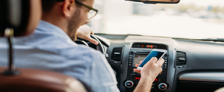 man driving while looking down on his phone