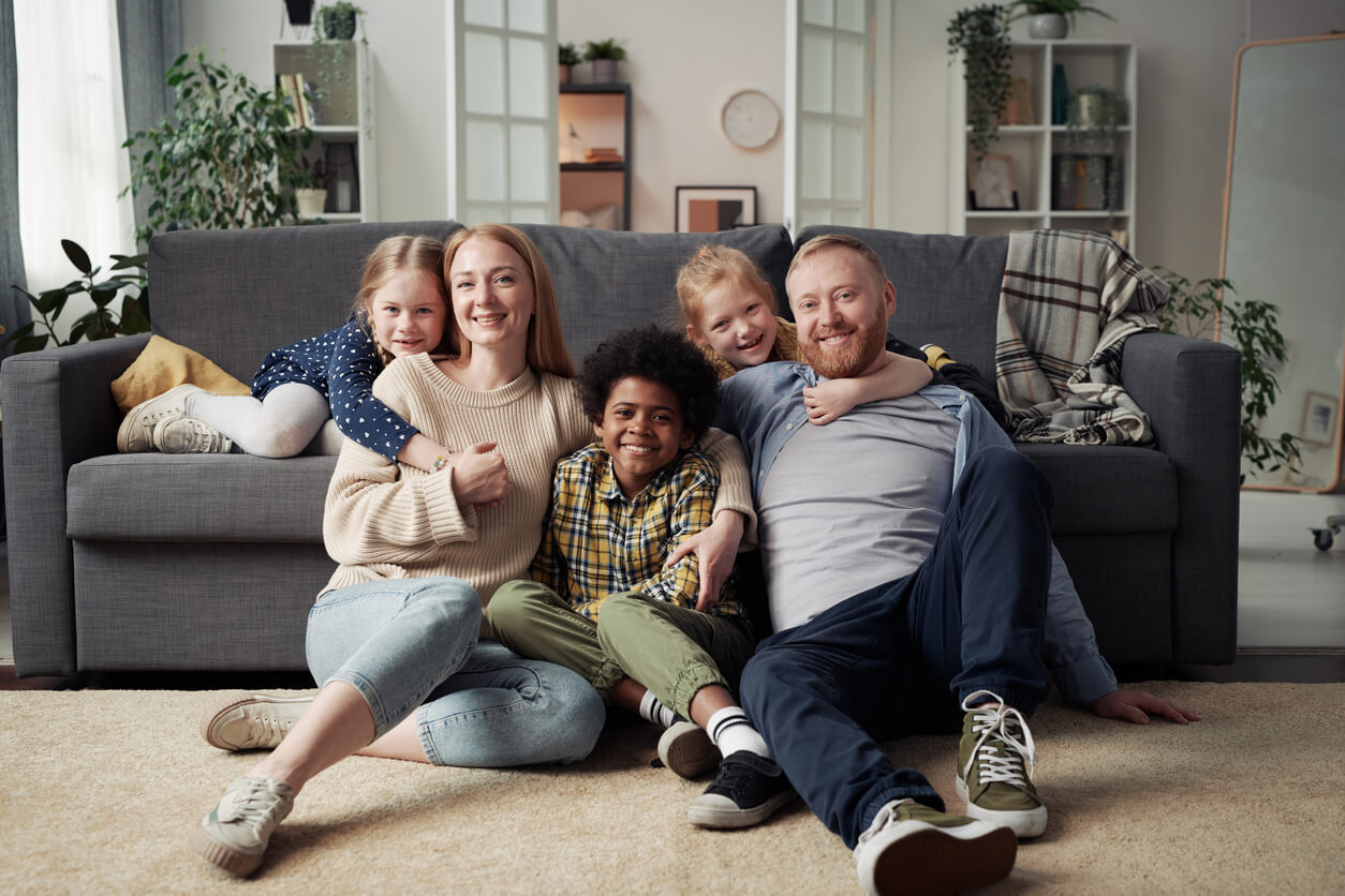 Portrait of happy parents with their adoptive children smiling at camera while resting together in living room at home