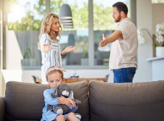 Kid feeling upset while parents argue in room. Couple arguing around child. Impact of family conflicts or divorce. Sad girl hugging teddybear