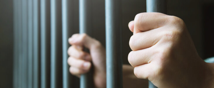 Man in prison hands of behind hold Steel cage jail bars. offender criminal locked in jail.