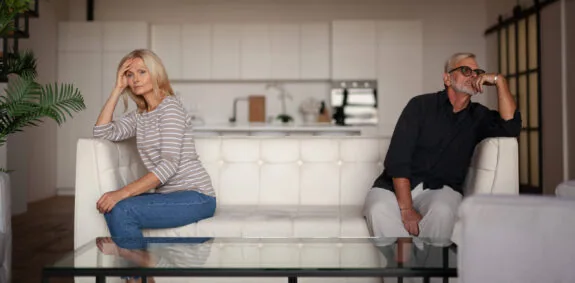 Quarrel and conflict in a mature family. Upset husband and wife are sitting on opposite sides of the sofa. Problems in the relationship between a man and a woman.